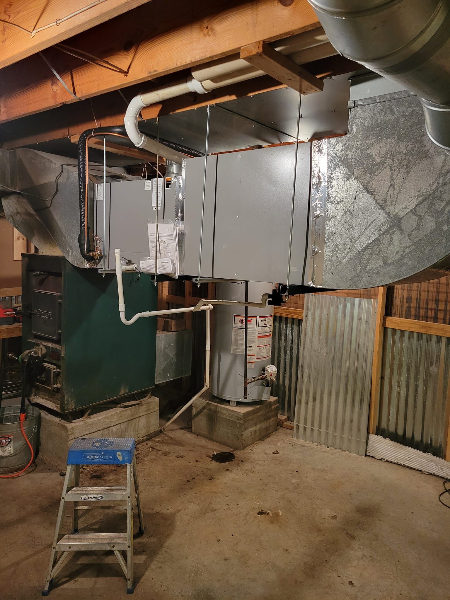 A ladder is sitting in a basement next to a furnace.