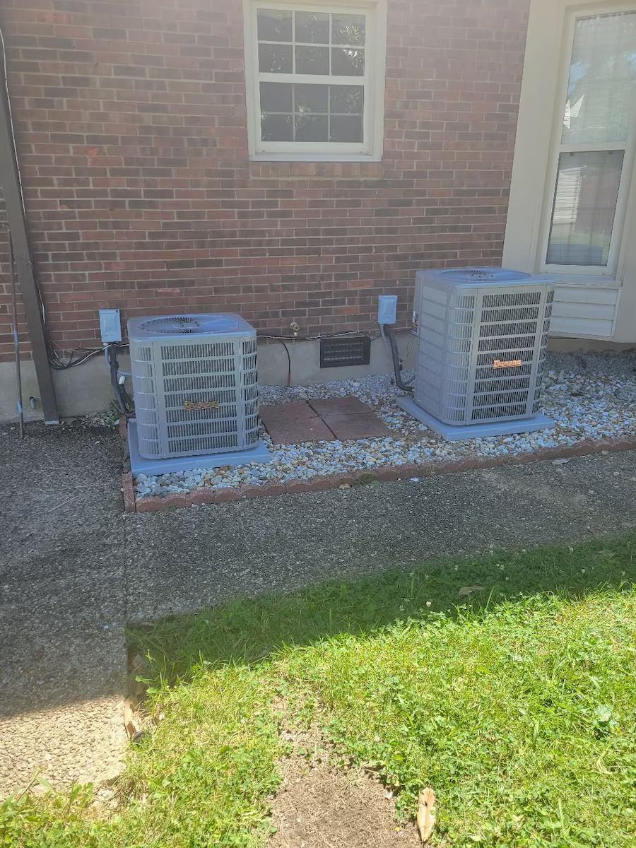 Two air conditioners are sitting on the side of a brick house.