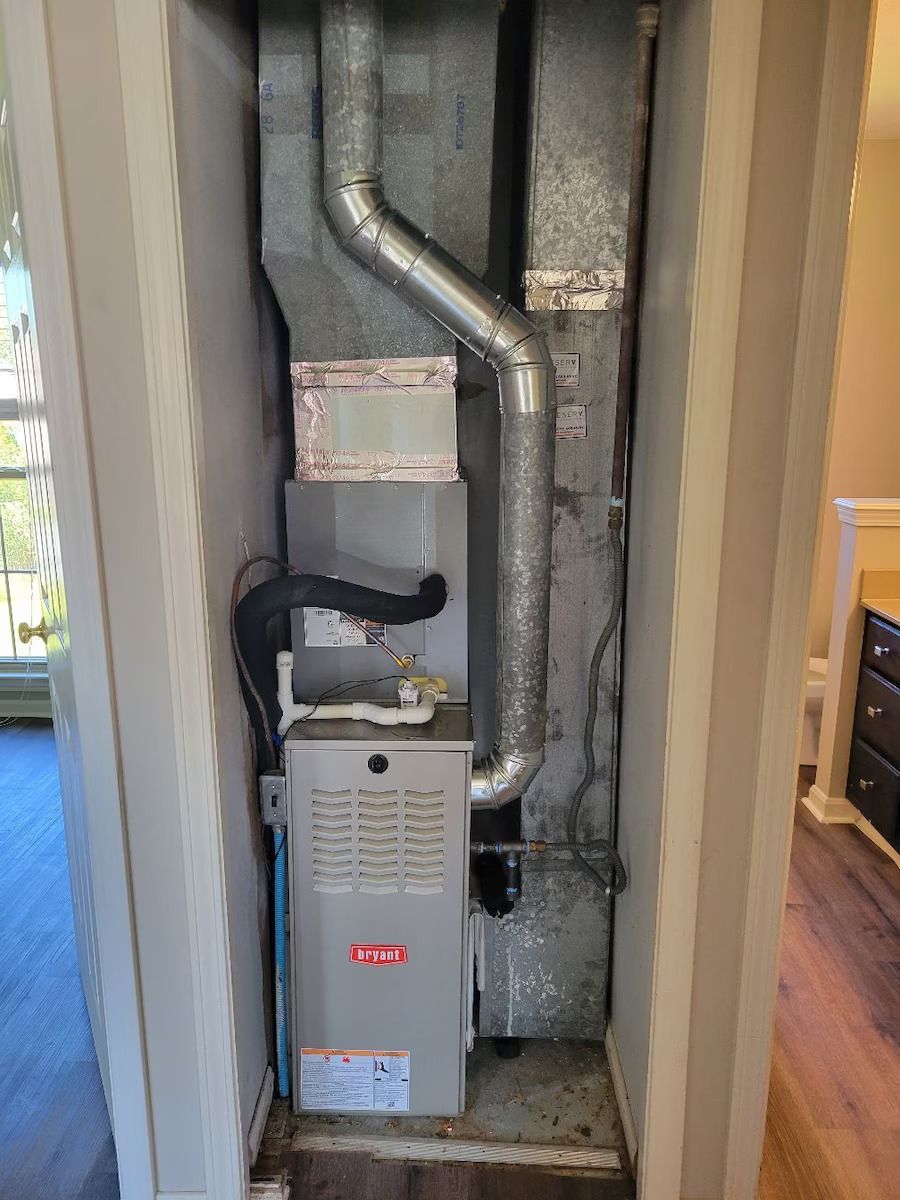 A furnace is sitting in a corner of a room next to a window.