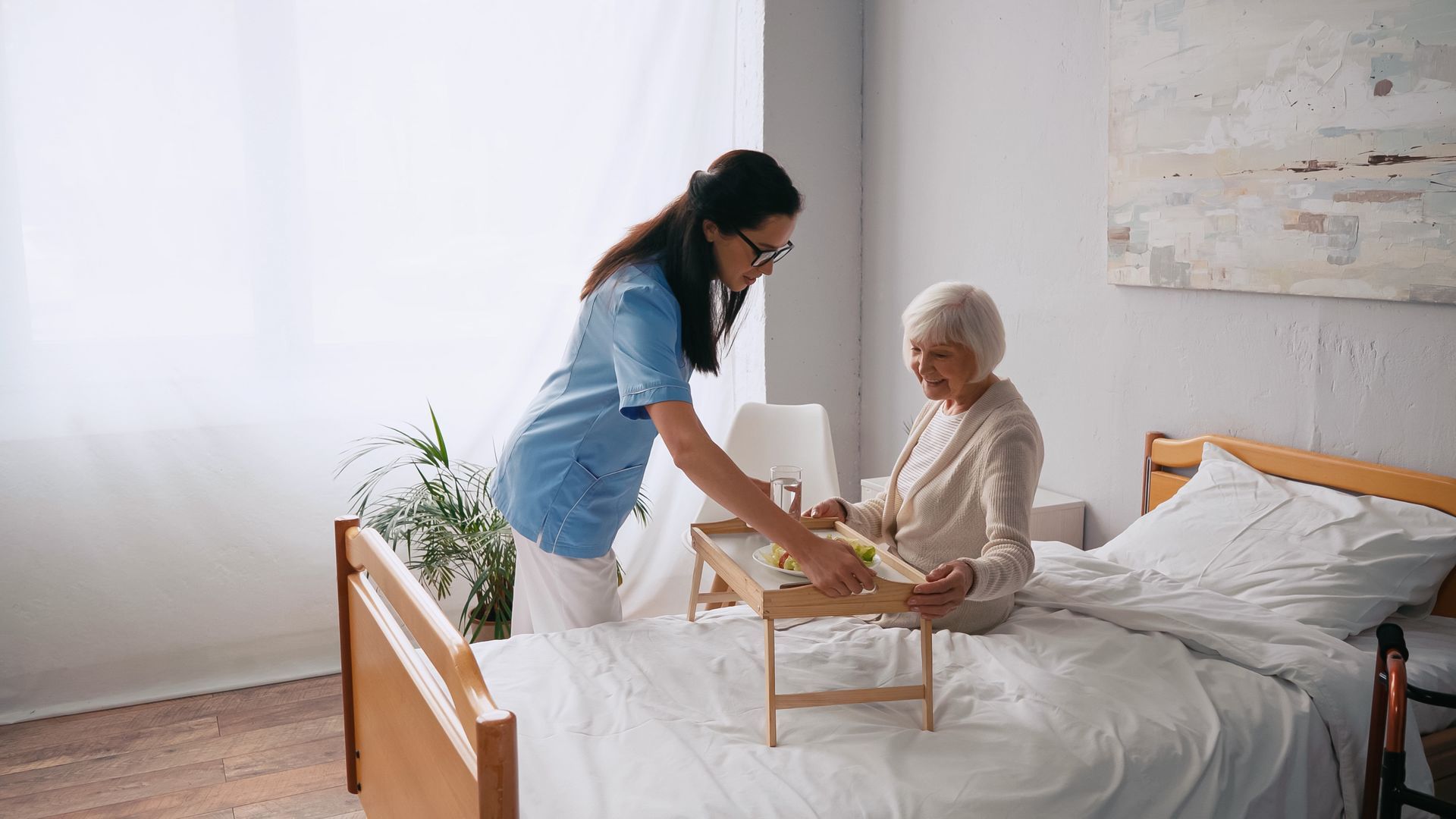 Caregiver serving breakfast to an elderly patient in a bright bedroom Caregiver serving breakfast to an elderly patient in a bright bedroom