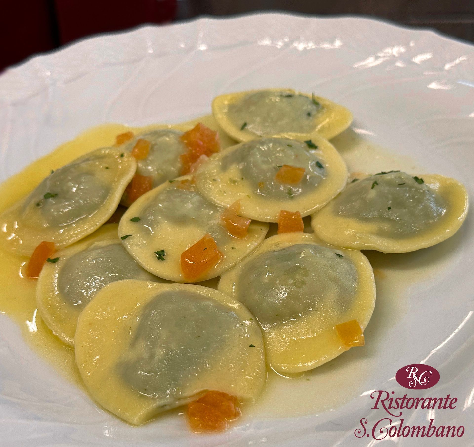 Una porzione di ravioli rotondi ripieni di verdure, serviti su un piatto bianco e guarniti con carote a dadini in una leggera salsa al burro.