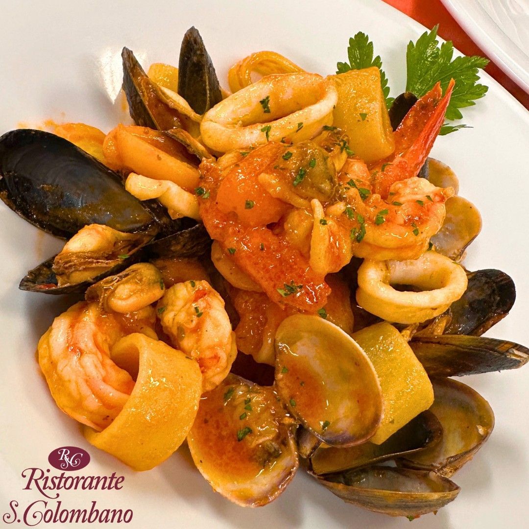 Un piatto di pasta ai frutti di mare con cozze, vongole, gamberi e calamari in una leggera salsa di pomodoro, guarnito con prezzemolo.