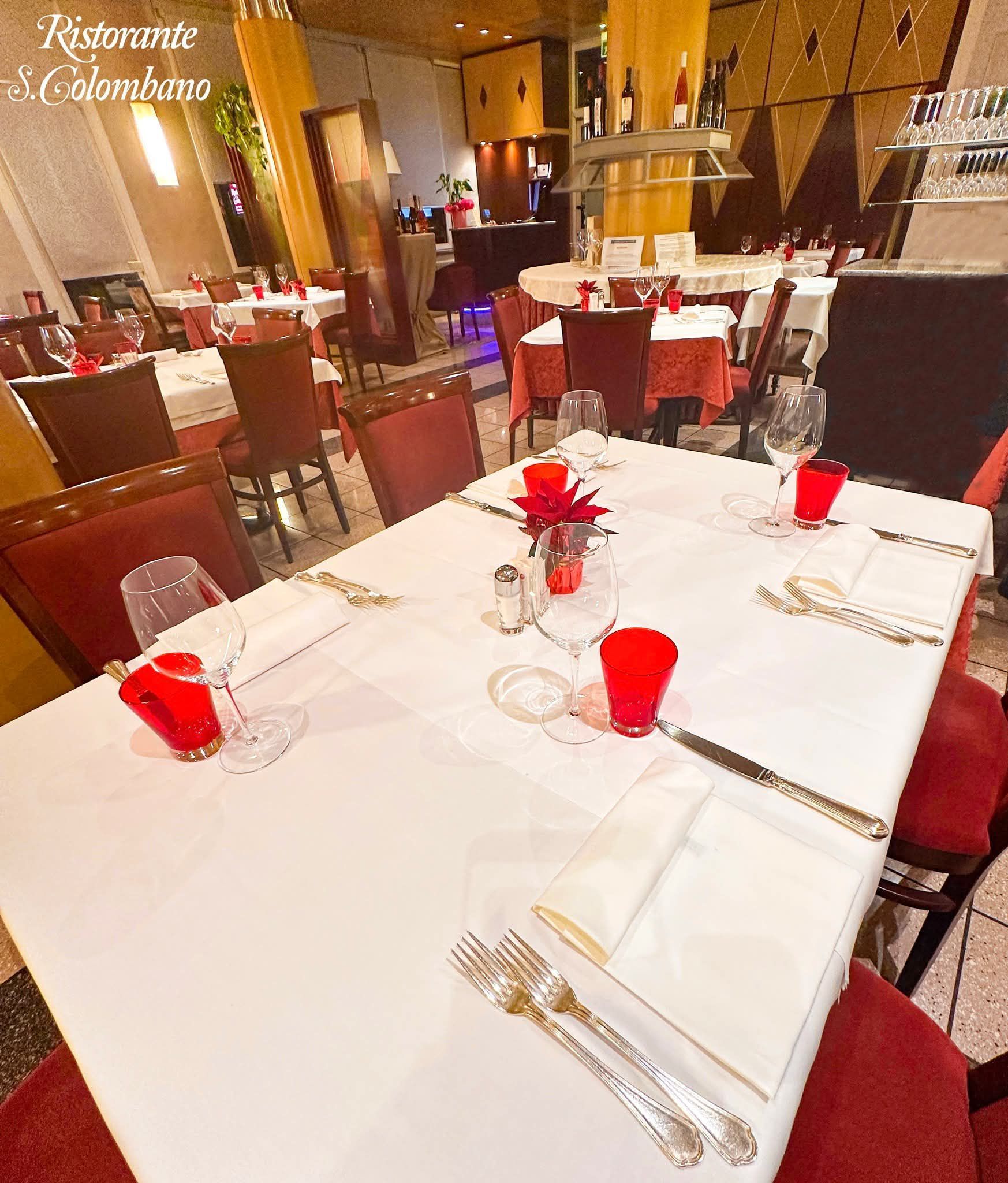Una sala da pranzo del Ristorante il Colombino con tavoli vuoti apparecchiati con tovaglie bianche, bicchieri rossi e sedie rosse.