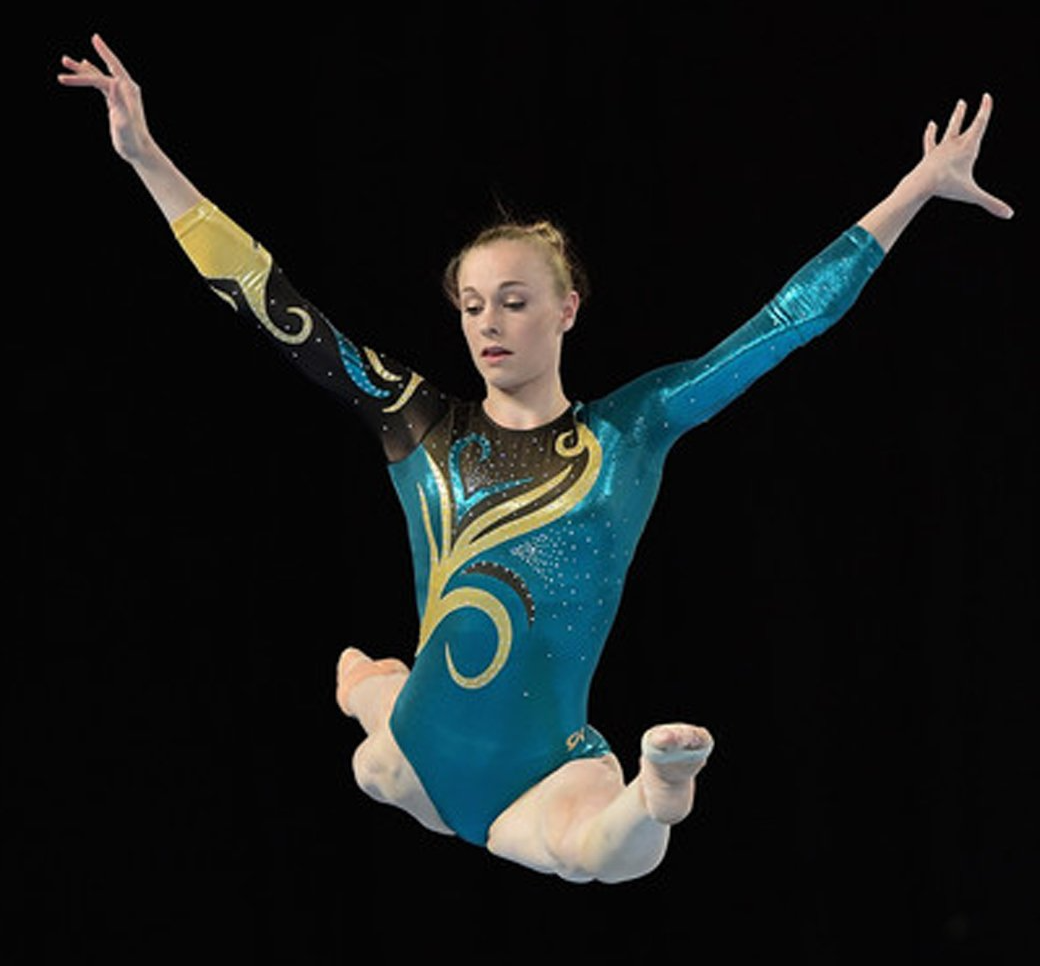 A female gymnast in a blue leotard is jumping in the air