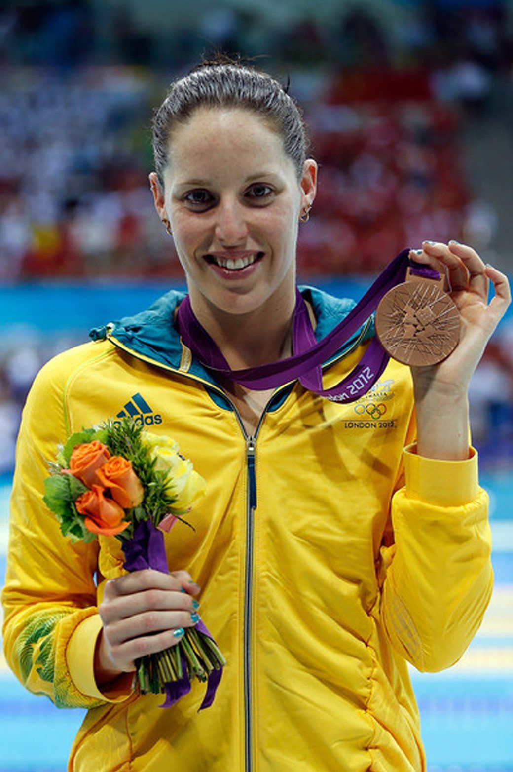 A woman in a yellow jacket is holding a medal and flowers.