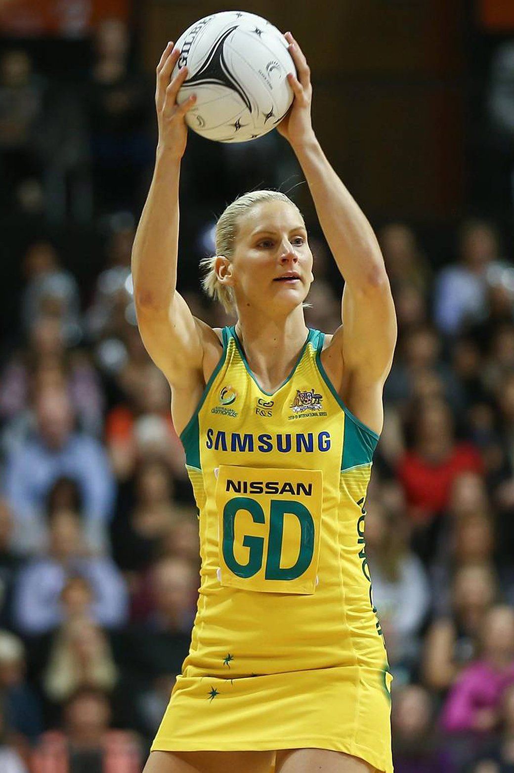 A woman in a yellow gd jersey is holding a ball