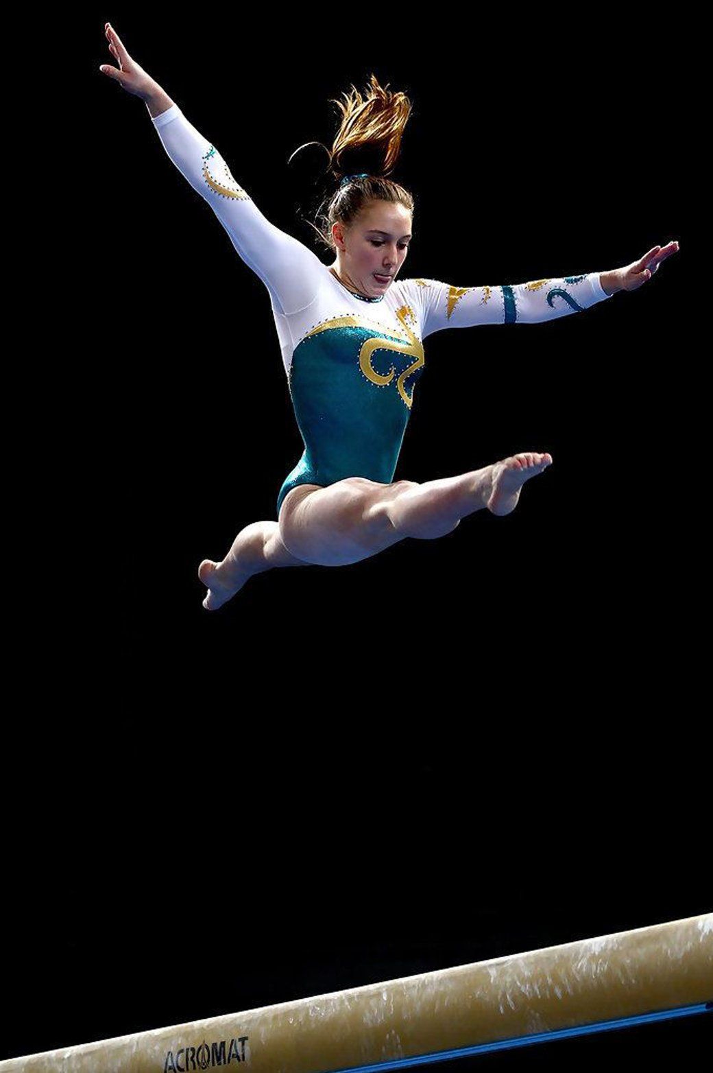 A female gymnast is jumping over a balance beam.