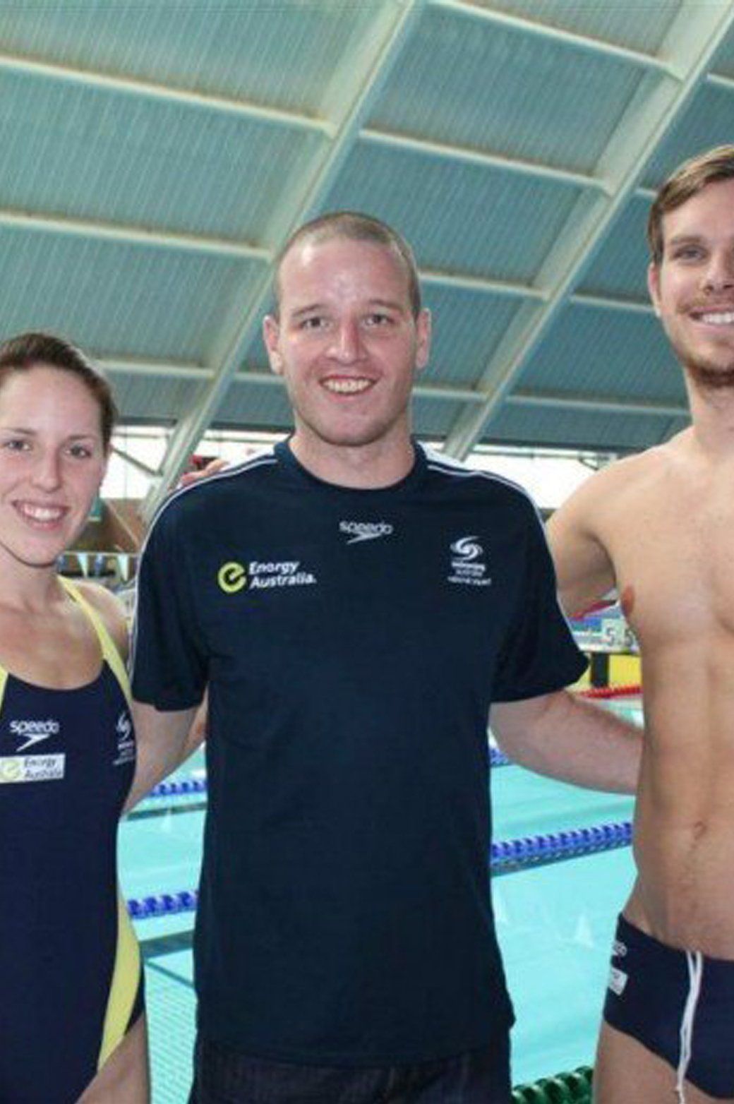 A man wearing a speedo shirt stands next to a woman and a man without a shirt