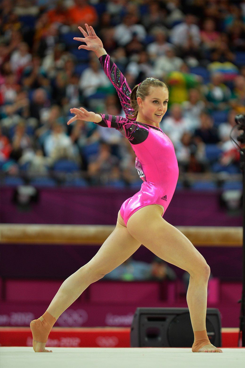 A female gymnast in a pink leotard is doing a routine on the floor.