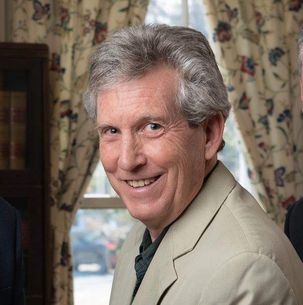 Michael A Fuerst in a tan suit is smiling in front of a window