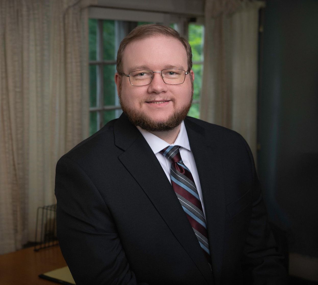 A man in a suit and tie is standing in front of a window.