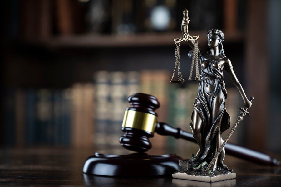 A statue of justice is sitting next to a wooden gavel on a wooden table.