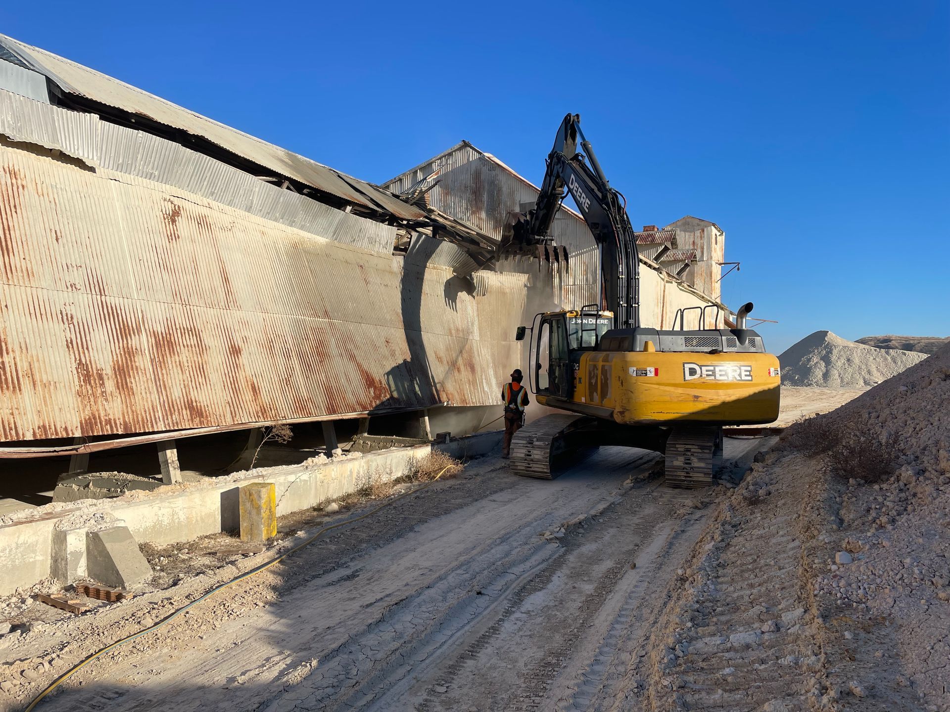 A Yellow Excavator Is Driving Down a Dirt Road in Front of a Building — Chicago, IL — Sterling Holloway Demolition