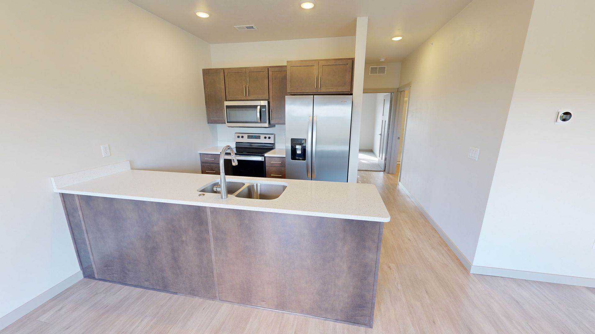 Modern kitchen with white island, wood cabinets, stainless appliances, and light wood flooring.