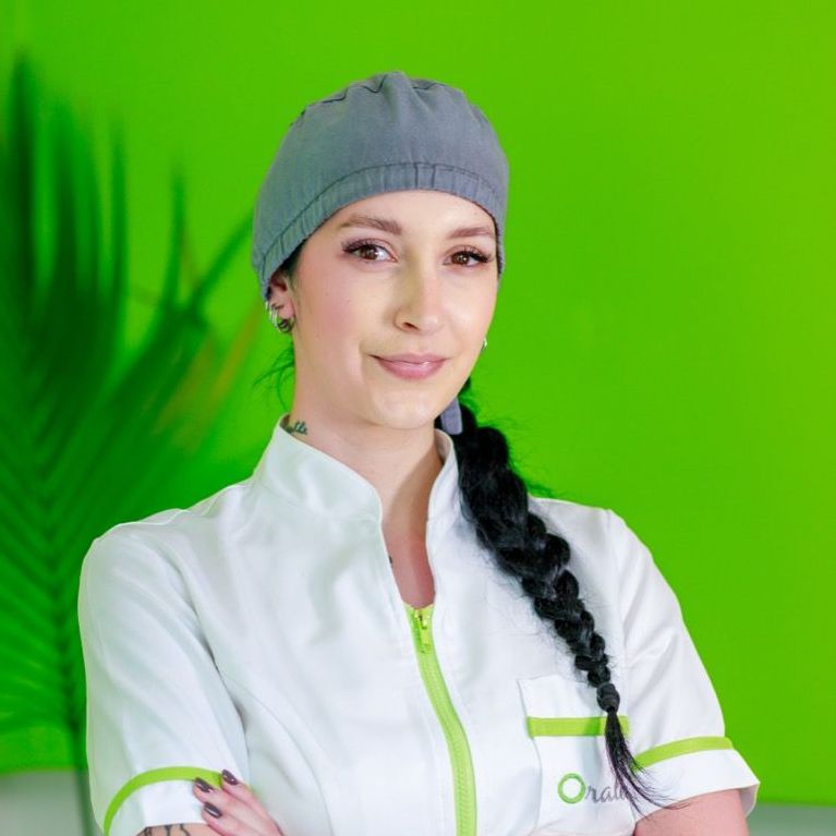 Una donna in camice bianco sorride con le braccia incrociate davanti a uno sfondo verde.