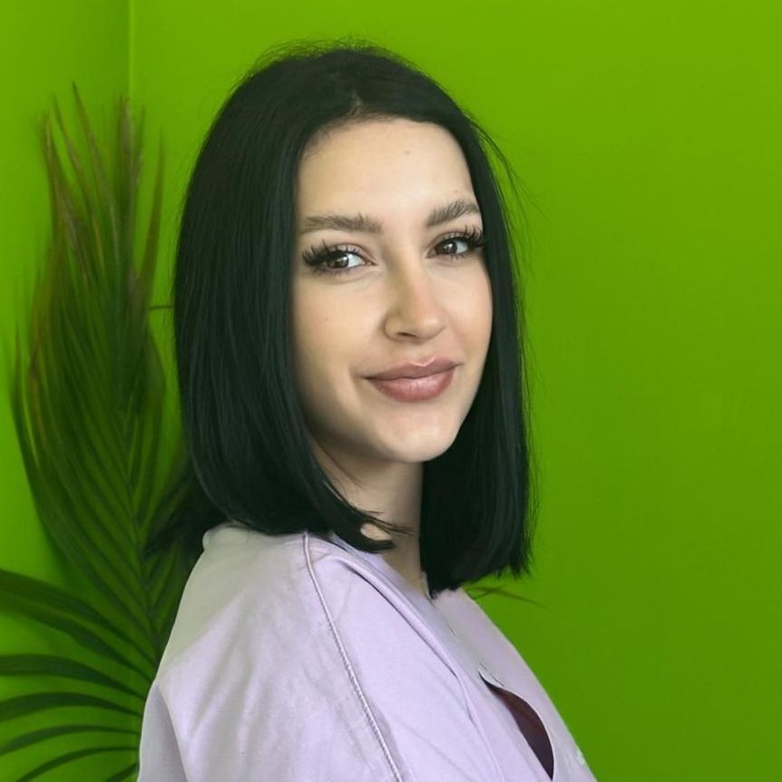 Una donna in camice bianco sorride con le braccia incrociate davanti a uno sfondo verde.