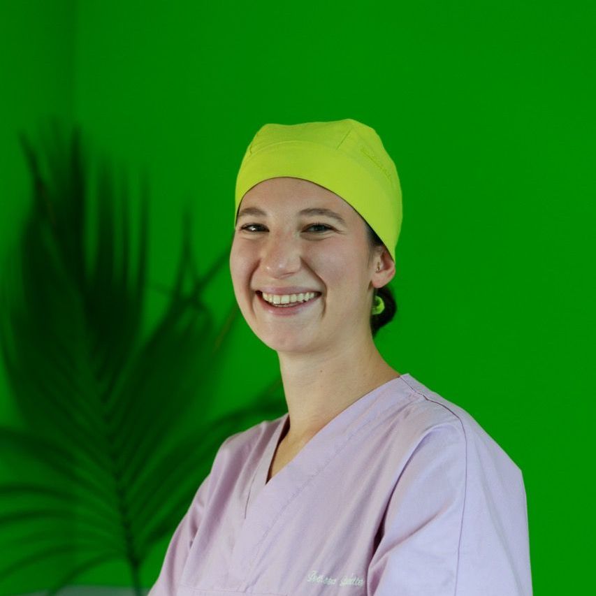 Una donna che indossa un cappello giallo e un camice sorride davanti a un muro verde.