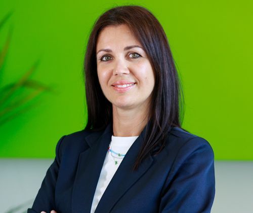 Una donna in giacca e cravatta è in piedi con le braccia incrociate davanti a un muro verde.