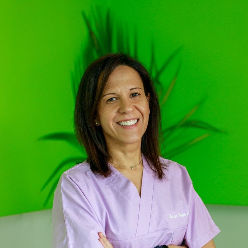 Una donna con un camice viola sorride davanti a un muro verde.