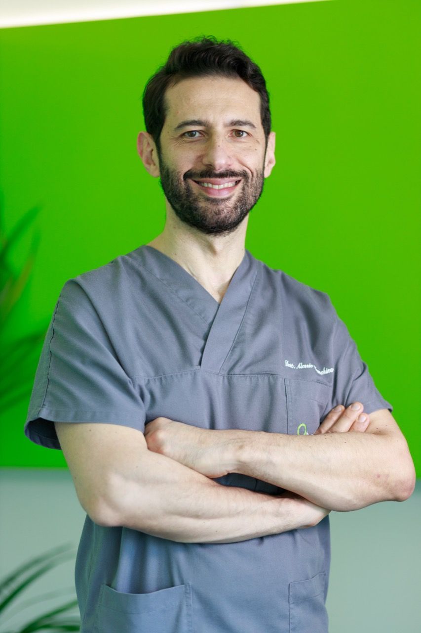 Dr. Alessio Franchina Un uomo in camice è in piedi con le braccia incrociate davanti a uno sfondo verde.