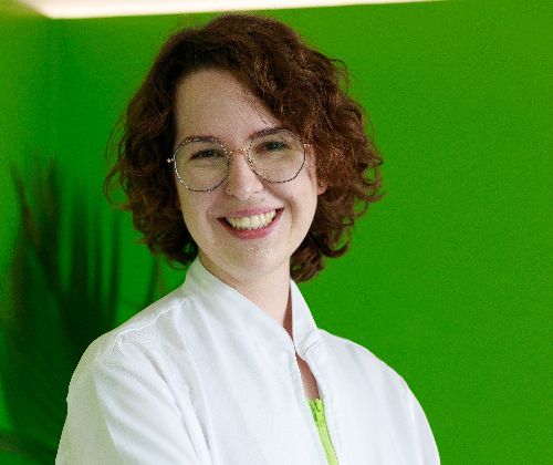 Una donna che indossa occhiali e camice bianco sorride davanti a un muro verde.