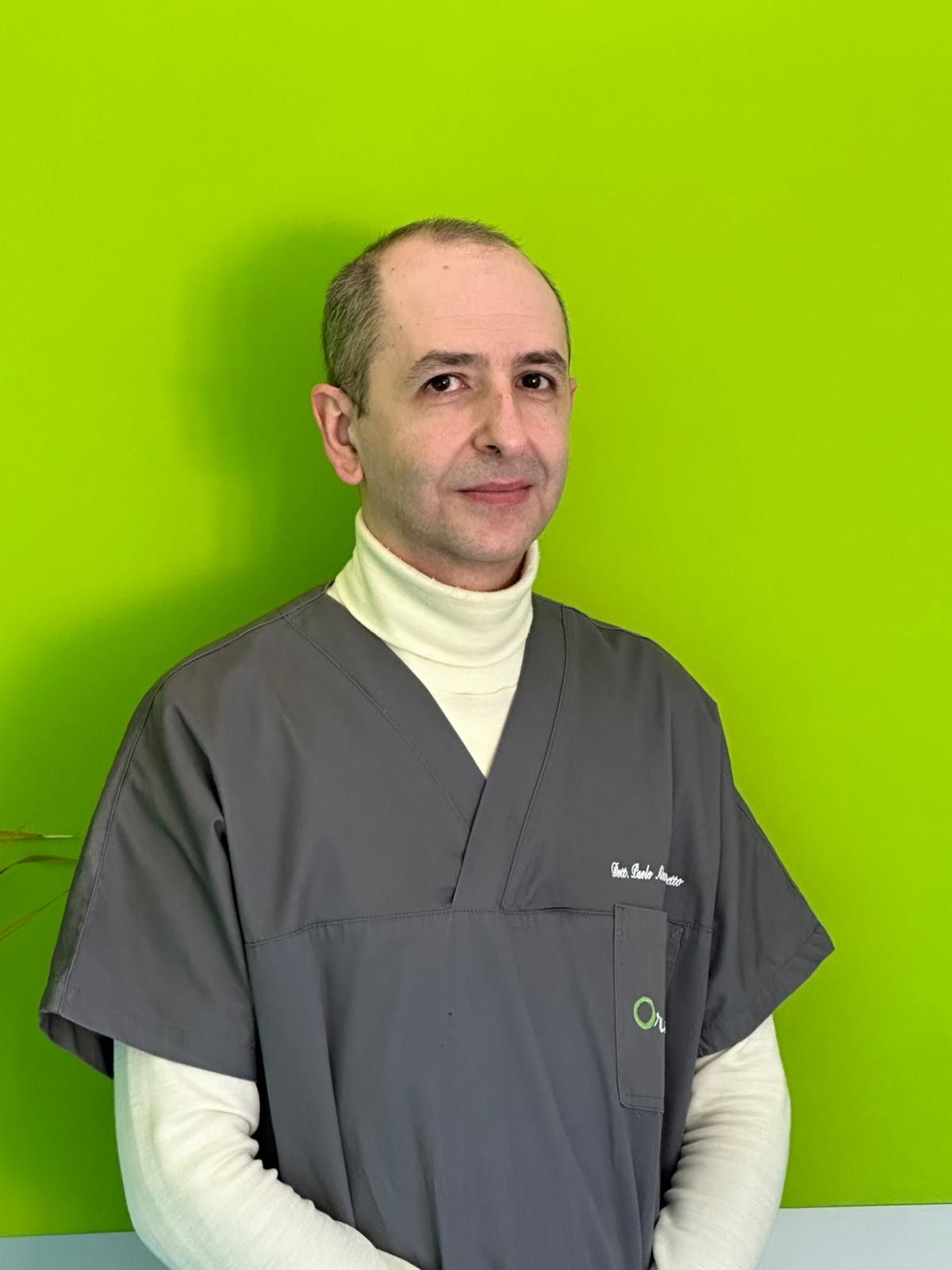 Un uomo in camice è in piedi con le braccia incrociate davanti a uno sfondo verde.