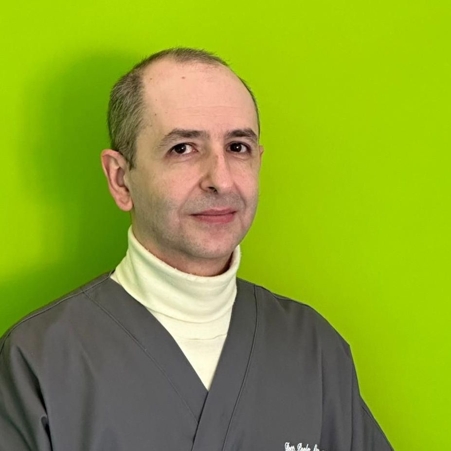 Un uomo con la barba indossa una camicetta e sorride davanti a un muro verde.
