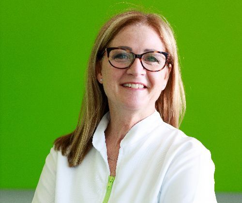 Una donna che indossa occhiali e camice bianco sorride davanti a uno sfondo verde.