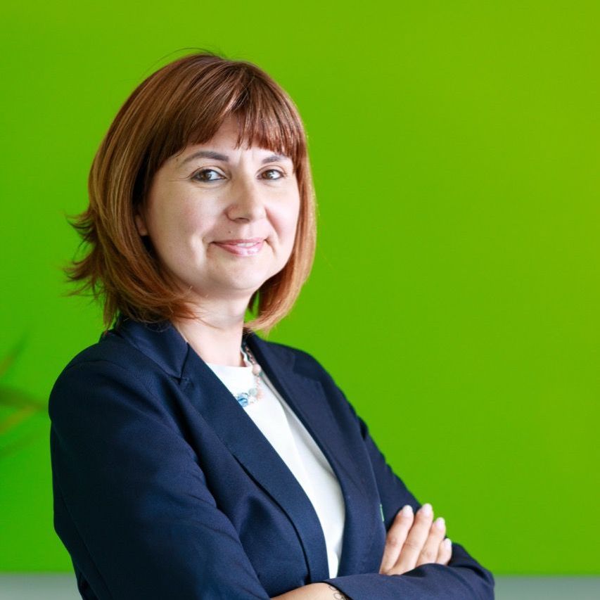 Una donna in giacca e cravatta è in piedi con le braccia incrociate davanti a un muro verde