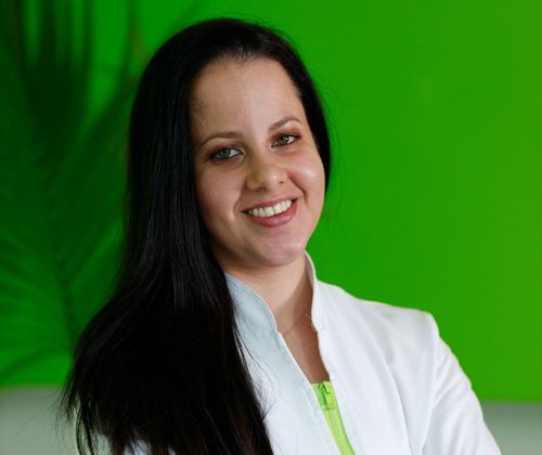 Una donna in camice bianco sorride davanti a uno sfondo verde.