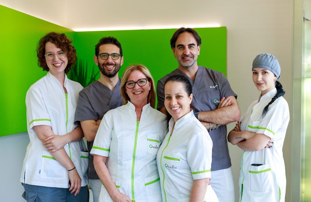 Un uomo in camice è in piedi con le braccia incrociate davanti a uno sfondo verde.