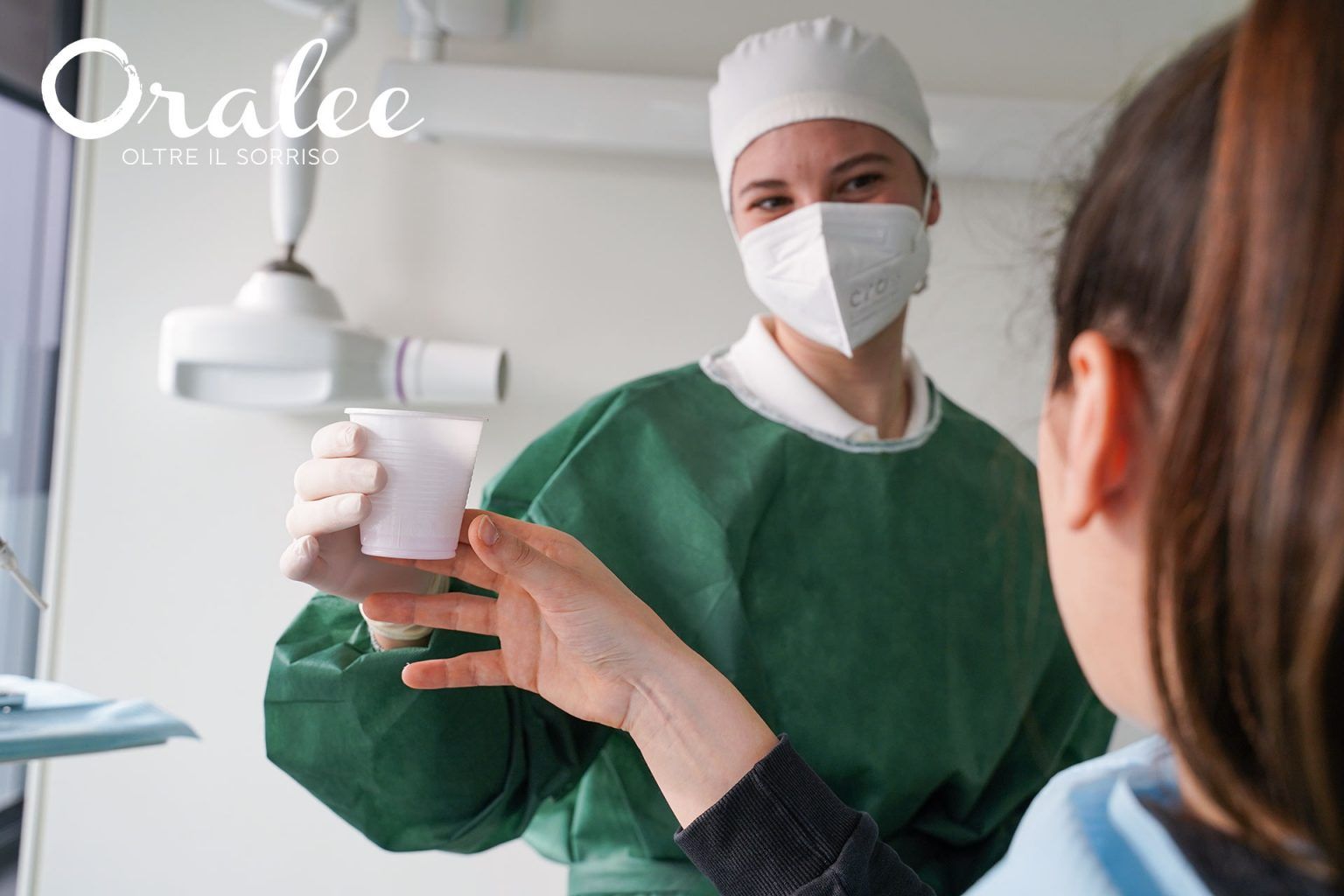 Una dentista che indossa una mascherina e un camice sta parlando con un paziente