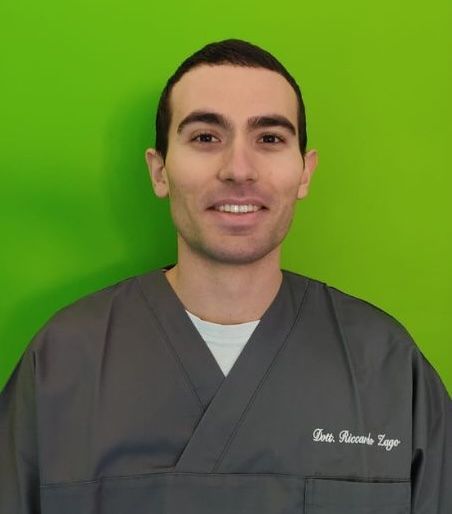 Un uomo in camice è in piedi con le braccia incrociate davanti a uno sfondo verde.