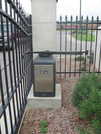 Gate opener with black arm attached to a black metal fence and a stainless steel box.