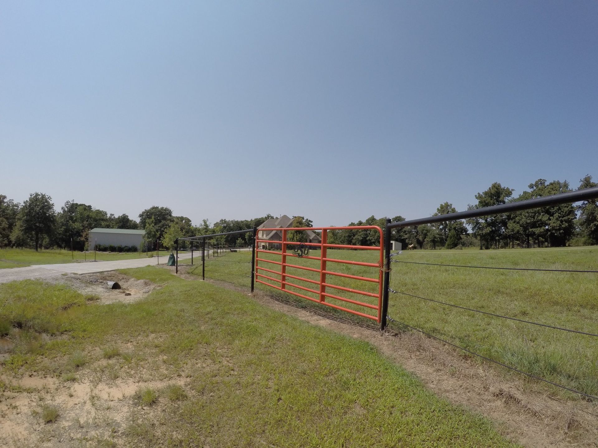 Orange gate open to a grassy field with trees under a blue sky.