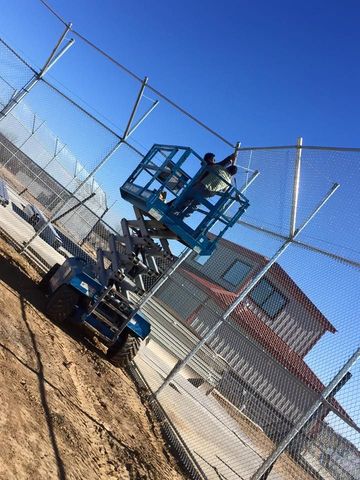 A worker on a blue lift installs fence in front of a building on a sunny day.