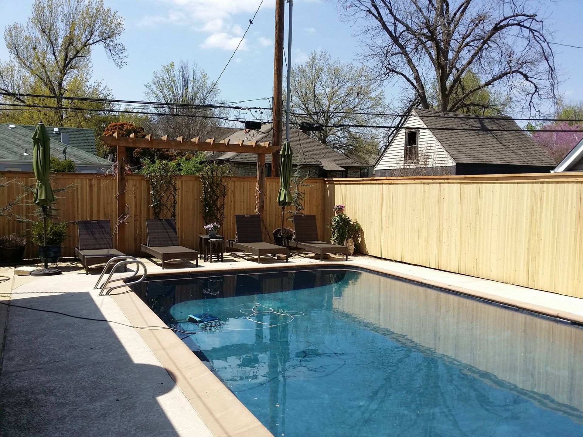 Swimming pool in backyard with lounge chairs, bamboo fence, and pergola.