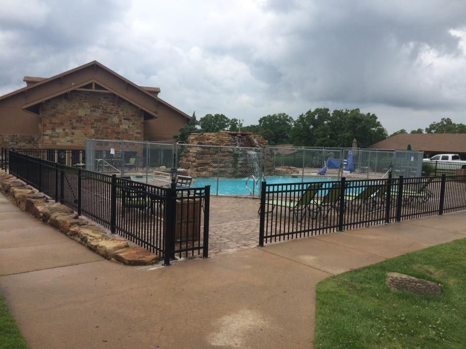 Pool area with a black fence, waterfall feature, and a cloudy sky.