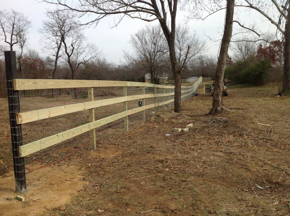 Wooden fence with three horizontal rails in a brown field with trees.