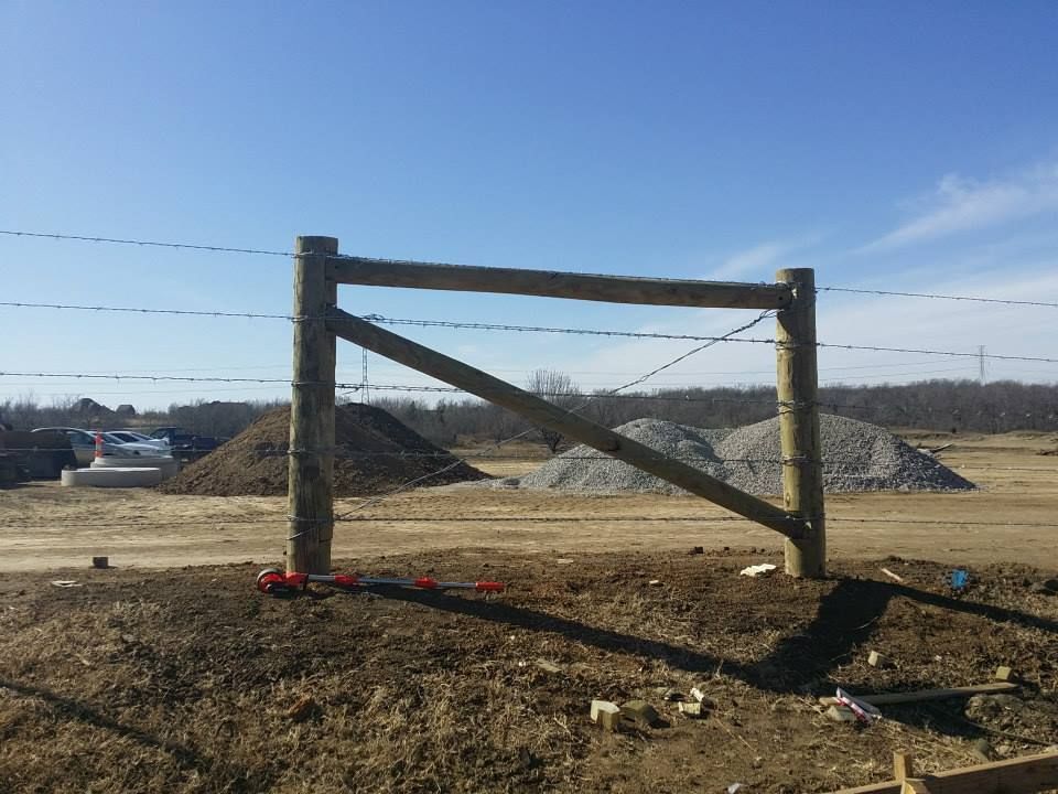 Wooden gate with barbed wire, set against a blue sky, in a construction area.