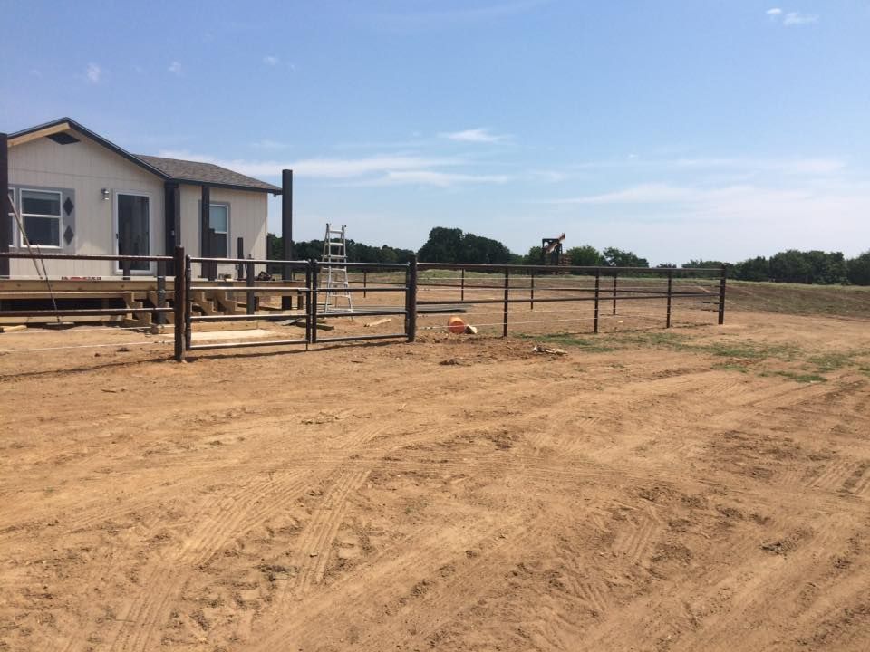 A small house with a wooden fence in a dirt yard on a sunny day.