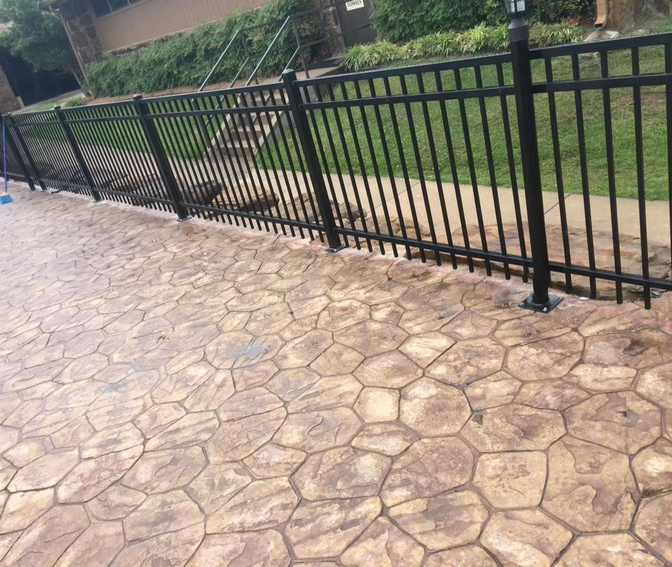 Black metal fence on patterned concrete by a pool.