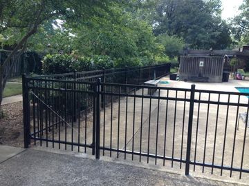 Black metal fence surrounding a pool area with a gate. Green trees in the background.