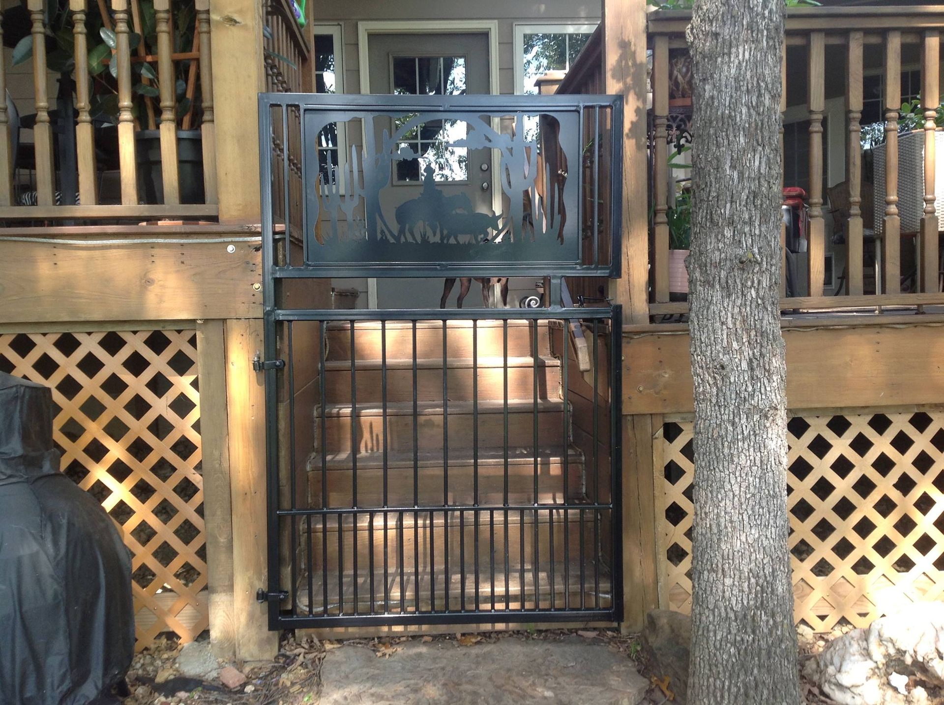 Black metal gate on wooden deck with decorative top, leading to outdoor steps.