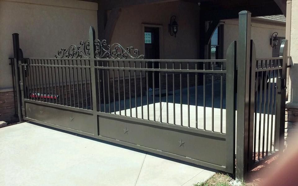 Brown metal gate blocking a driveway.  Scrollwork top, vertical bars. Concrete surface, stucco wall background.