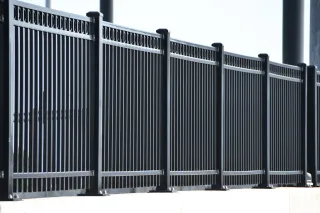 Chain-link fence topped with razor wire against a blue sky with clouds.