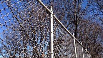 Chain-link fence topped with razor wire against a blue sky with clouds.