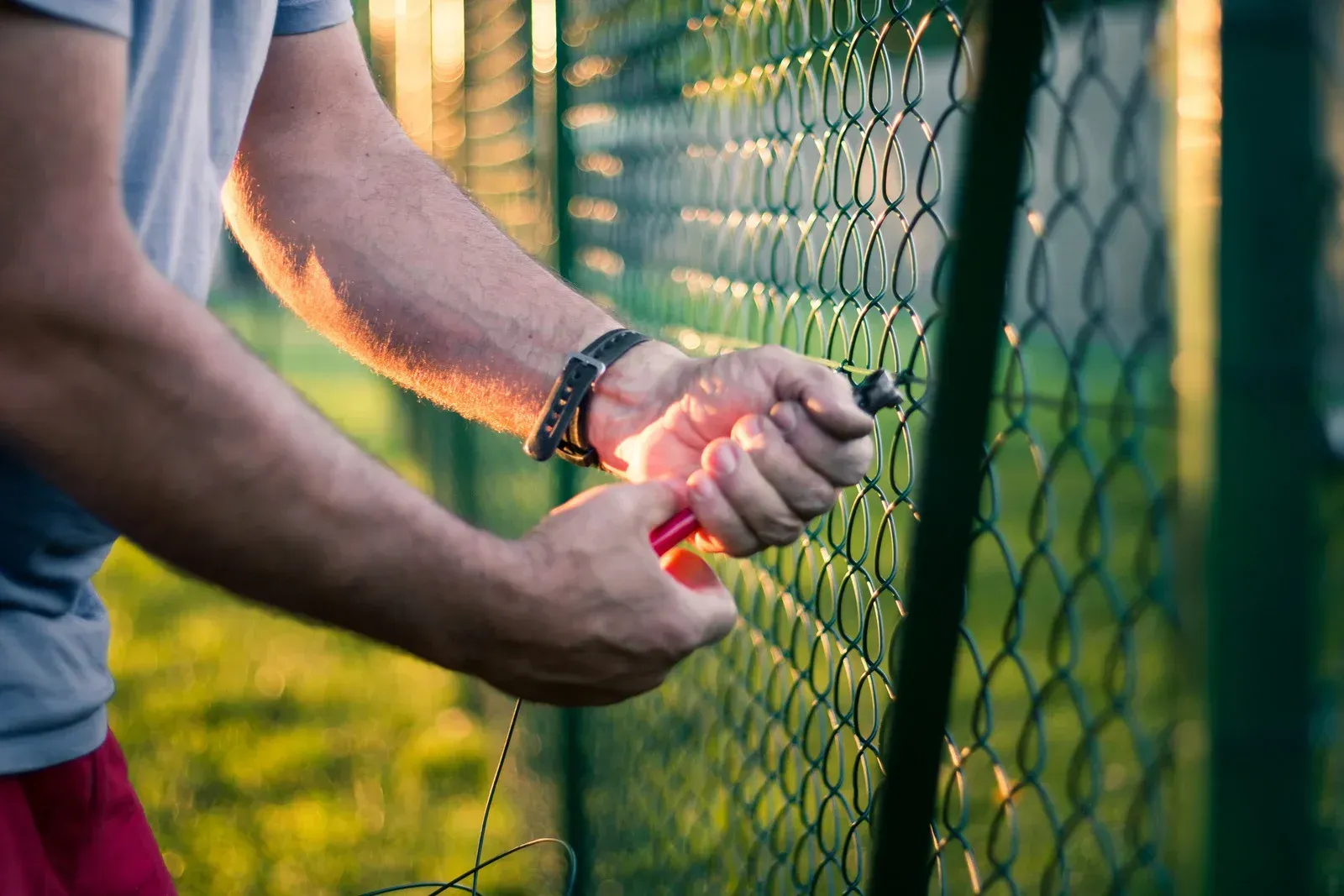 Chain-link fence topped with razor wire against a blue sky with clouds.