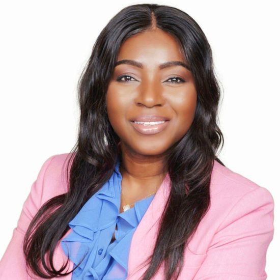 Woman with long black hair, smiling, wearing a pink blazer and blue blouse.
