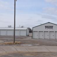 Midtown Storage facility with white metal buildings and multiple storage unit doors under a pale blue sky.